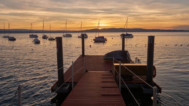 Bodensee Lake Panorama. Evening, twilight, setting sun, picturesque landscape, serene waters, boats and yachts at the dock, beautiful sky with clouds reflecting in the water, riverside at dusk, showcasing the coexistence of technology and production with the environment.