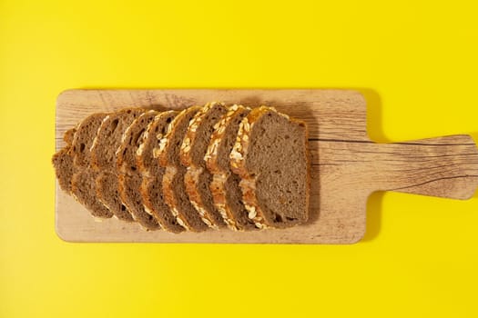 Top view of sliced wholegrain bread on a wooden cutting board on a yellow background.