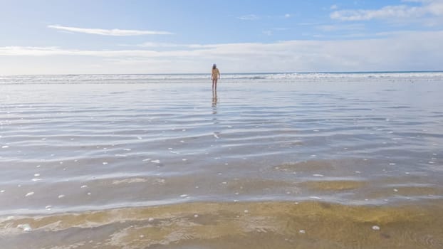 Little girl, braving the cold, joyfully runs in her swimsuit across the beach during winter.