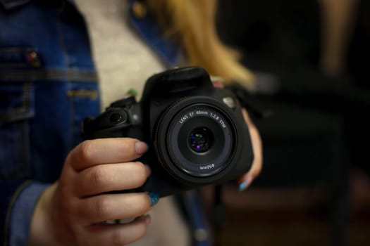 A girl in a blue denim jacket holds a black camera in her hand in close-up