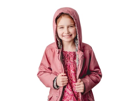 Little girl in pink jacket smiling at camera while standing indoors on white wall background