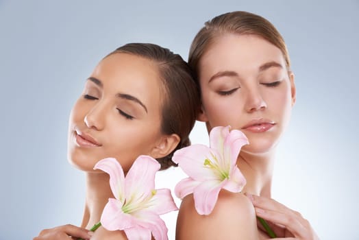 Woman, relax and skincare with flowers for natural beauty, makeup or cosmetics on a blue studio background. Young female, people or models smile in satisfaction for spa, soft skin or facial treatment.