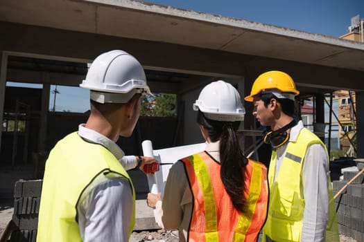 Team of professional civil engineers and architects holding project plan paper, supervising and controlling construction project work at construction site..