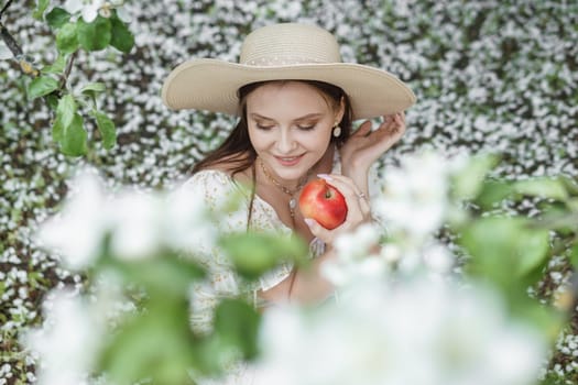 An attractive long-haired woman walks in the spring in the park of blooming apple trees. Spring portrait of a woman