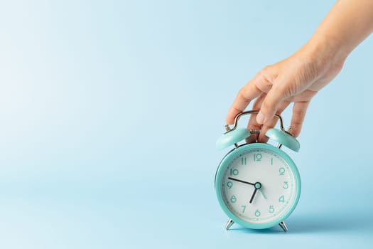 A person, likely a woman, holds an alarm clock in her hand, emphasizing the concept of time, deadlines, and the stress associated with managing work hours