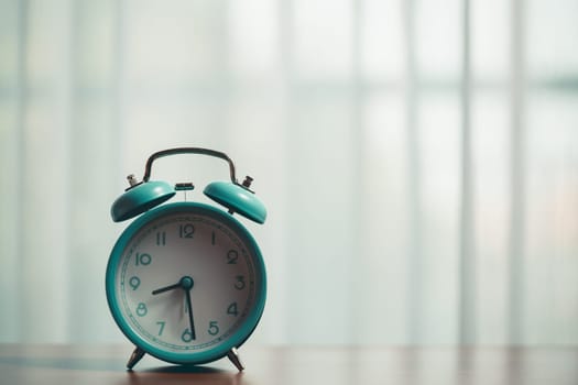 Table with a vintage alarm clock, set against the curtains with morning sunlight shining on, showcasing a classic metal timepiece with retro charm and a sense of urgency