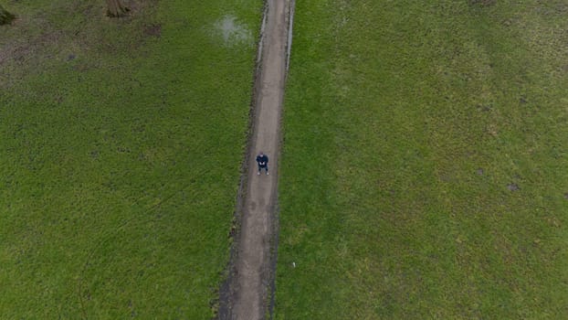 Aerial view of man flying a drone or UAV , standing on a trqack in a green field with grass