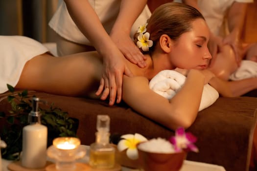 Caucasian couple customer enjoying relaxing anti-stress spa massage and pampering with beauty skin recreation leisure in warm candle lighting ambient salon spa at luxury resort or hotel. Quiescent