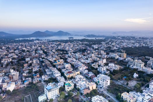 Aerial drone shot over udiapur, jaipur, kota,, cityscape with homes, houses, buildings and aravalli hills and lakes in the distance hidden in fog in India