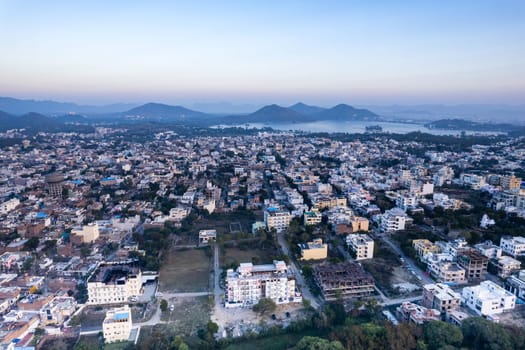 Aerial drone shot over udiapur, jaipur, kota,, cityscape with homes, houses, buildings and aravalli hills and lakes in the distance hidden in fog in India