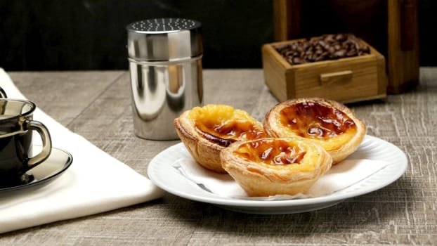 Pasteis de Nata or Portuguese Custard Tarts with black coffee on wooden table.