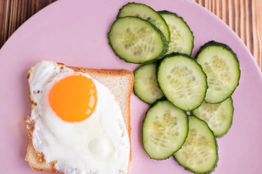 toast with egg on a plate. Fresh cucumbers. slice of white bread on a pink background. sandwich. breakfast with fried egg. High quality photo