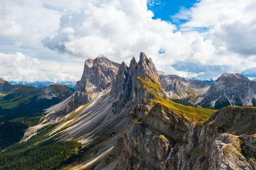 Observation point on slope overlooking bare peak of Seceda mountain in Italian Alps. Rocky ridgeline under cumulus clouds highland aerial view
