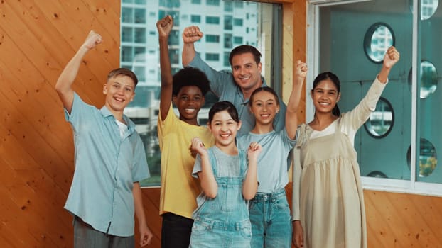 Smart teacher and diverse student standing while waving hand to camera. Skilled instructor with highschool children with mixed races in casual outfit greeting and smiling with cheerful. Edification.