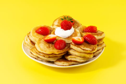 Mini pancakes with strawberries and sour cream on a yellow background.