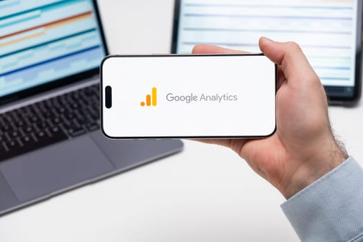 PRAGUE, CZECH REPUBLIC - JANUARY 21 2024: Google Analytics logo on the screen of a cell phone in business mans hand and laptop on the background.