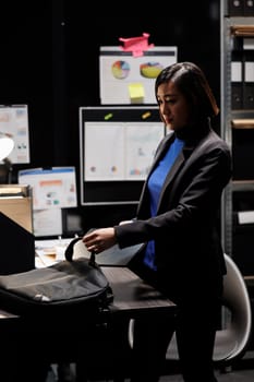 Businesswoman packing laptop up in office suitcase bag clocking out from storage room office. Bookkeeping asian executive in business accountancy company file cabinet depository