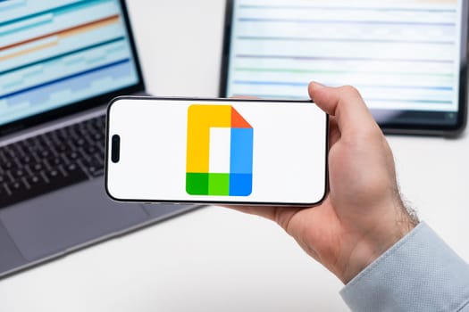 PRAGUE, CZECH REPUBLIC - JANUARY 21 2024: Google Docs logo on the screen of a cell phone in business mans hand and laptop on the background.