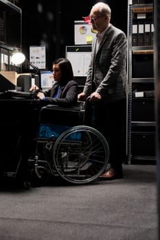 Paralyzed asian businesswoman executive sitting in wheelchair at office desk, inspecting quarterly results analysis data on laptop. Woman with paraplegia in accountancy workplace