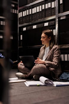 Businesswoman analyzing bookkeeping report, searching files with administrative research in corporate depository. Diverse employees working late at night in arhive room, reading management record