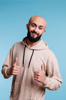 Cheerful arab man showing approval gesture with two thumbs up portrait. Smiling person with joyful facial expression standing with satisfaction sign while looking at camera