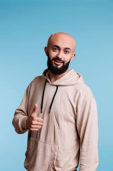 Smiling arab man expressing satisfaction with thumb up gesture portrait. Young happy handsome person with carefree emotions showing approval and agreement while looking at camera
