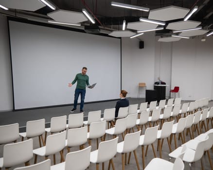 A red-haired Caucasian businesswoman sits in the front row of an empty conference room. Bearded man giving a lecture