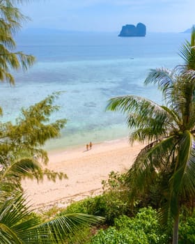 view between palm tree leaves at a couple of men and woman on the beach at Koh Ngai island Thailand, with palm trees and soft white sand, and a turqouse colored ocean in Koh Ngai Trang Thailand