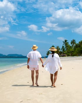 a young couple of caucasian men and a Thai Asian woman walking at the beach of Koh Muk a tropical island, with palm trees soft white sand, and a turqouse colored ocean Koh Mook Trang Thailand