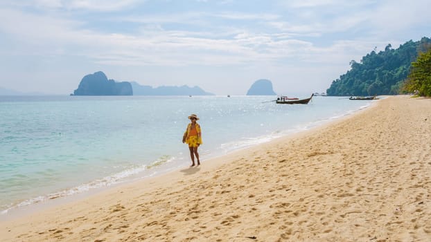 woman walking at the beach at Koh Ngai island with palm trees and soft white sand, and a turqouse colored ocean in Koh Ngai Trang Thailand