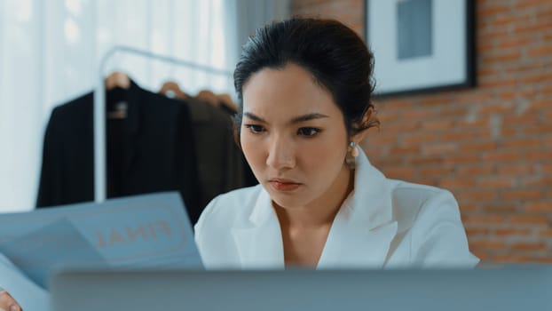 Young businesswoman sitting on the workspace desk using laptop computer for internet online content writing or remote working from home. Clothing and textile business marketing analysis. Vivancy