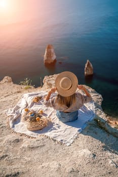 woman sea travel. photo of a beautiful woman with long blond hair in a pink shirt and denim shorts and a hat having a picnic on a hill overlooking the sea.