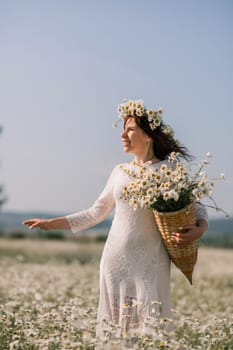 Happy woman in a field of daisies with a wreath of wildflowers on her head. woman in a white dress in a field of white flowers. Charming woman with a bouquet of daisies, tender summer photo.