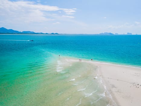 a couple of men and woman walking at a sandbar in the ocean of Koh Muk a tropical island with palm trees and soft white sand, and a turqouse colored ocean in Koh Mook Trang Thailand