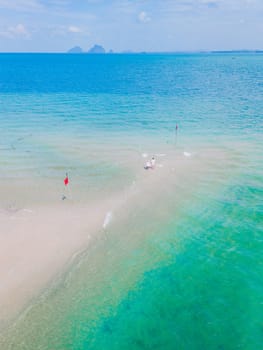 a couple of men and woman walking at a sandbar in the ocean of Koh Muk a tropical island with palm trees and soft white sand, and a turqouse colored ocean in Koh Mook Trang Thailand