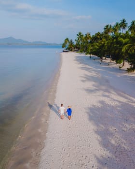 Drone view at a couple walking on the white sandy tropical beach of Koh Muk with palm trees soft white sand, and a turqouse colored ocean in Koh Mook Trang Thailand on a sunny afternoon