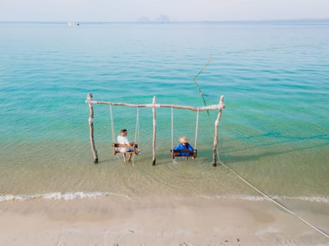 a couple of men and a woman on a swing at the beach of Koh Muk tropical island , and a turqouse colored ocean in Koh Mook Trang Thailand, a couple on a swing in the ocean