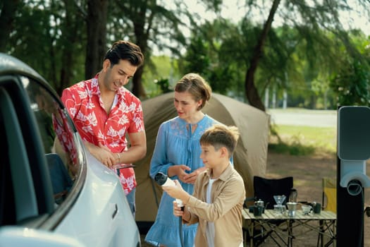 Outdoor adventure and family vacation camping in nature travel by eco friendly car for sustainable future. Lovely family recharge EV car with EV charging station in campsite. Perpetual