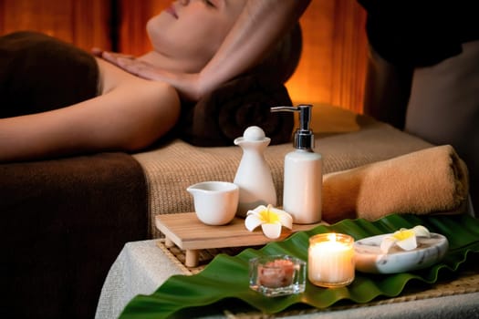 Aromatherapy massage ambiance or spa salon composition setup with focus decor candles and spa accessories on blurred woman enjoying blissful aroma spa massage in resort or hotel background. Quiescent