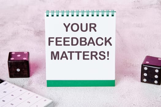 YOUR FEEDBACK MATTERS text on a white notepad sheet next to dice on an abstract background