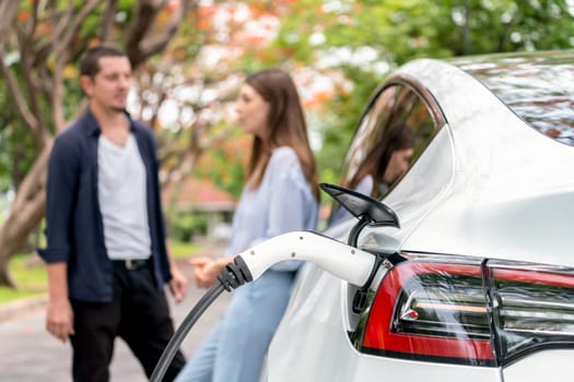 Lovely young couple recharging battery for electric car during autumnal road trip travel EV car in autumnal forest. Eco friendly travel on vacation during autumn. Exalt