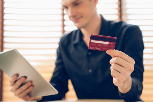 Young man using tablet with credit card for internet banking, online shopping E commerce by online payment gateway at home office. Modern and convenience online purchasing with debit card. Unveiling