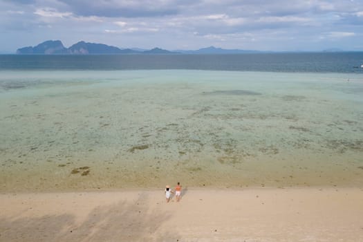 oh Kradan a tropical island with palm trees soft white sand, and a turqouse colored ocean, couple standing by the ocean in Koh Kradan Trang Thailand