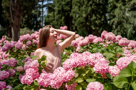 Hydrangeas Happy woman in pink dress amid hydrangeas. Large pink hydrangea caps surround woman. Sunny outdoor setting. Showcasing happy woman amid hydrangea bloom