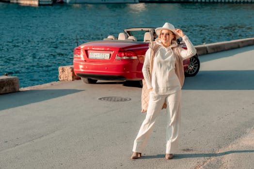 Portrait of a blonde convertible. Fashionable attractive woman with blond hair in a white hat on the background of a red car and the sea