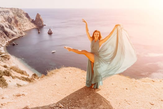 Woman green dress sea. Female dancer posing on a rocky outcrop high above the sea. Girl on the nature on blue sky background. Fashion photo