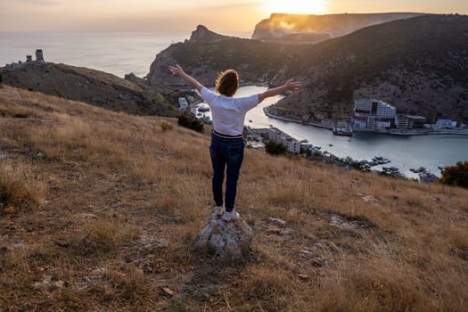 Happy woman on sunset in mountains. Woman standing with her back on the sunset in nature in summer with open hands. Silhouette