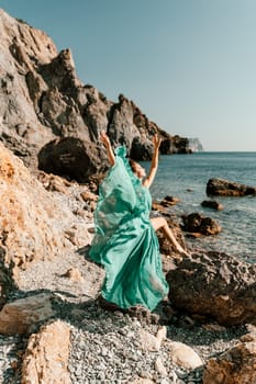 Woman green dress sea. Woman in a long mint dress posing on a beach with rocks on sunny day. Girl on the nature on blue sky background