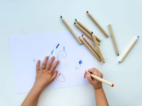 small child draws with colored pencils on paper on white table. High quality photo