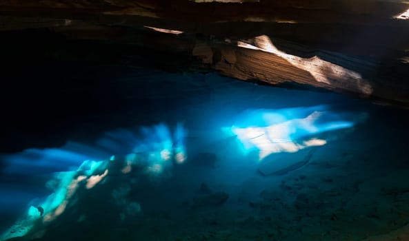 Sunlight streams through a cave, lighting up the blue waters beneath.